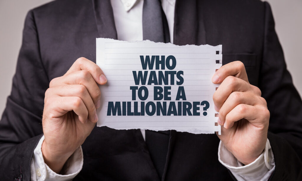 suited man holding sign saying Who Wants To Be A Millionaire?'