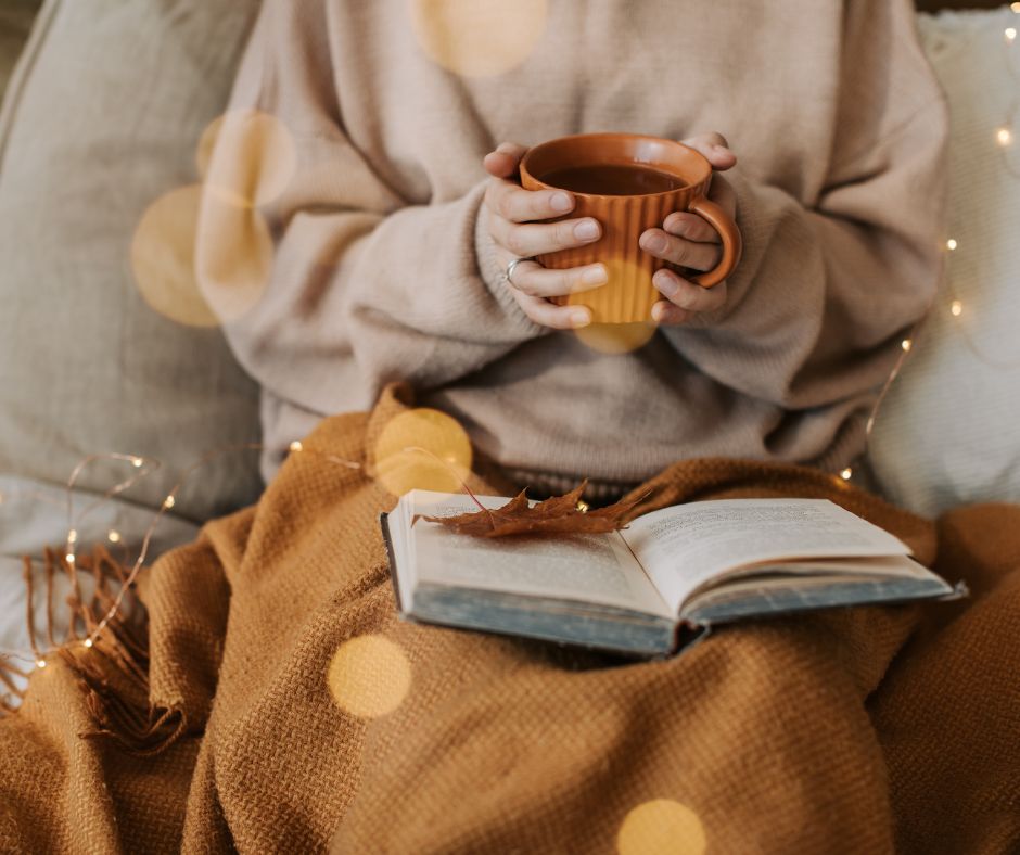 woman keeping warm with blanket and hot drink reading a book