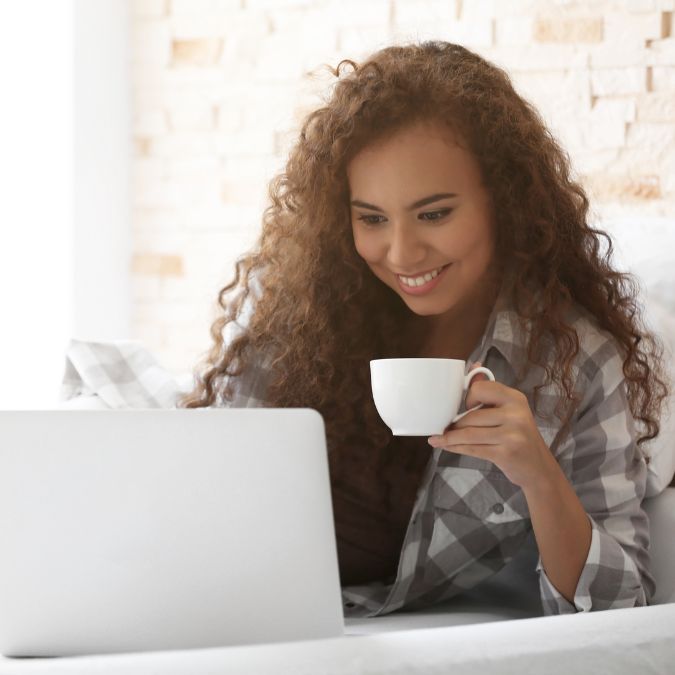 woman happy on laptop with cup of coffee in hand