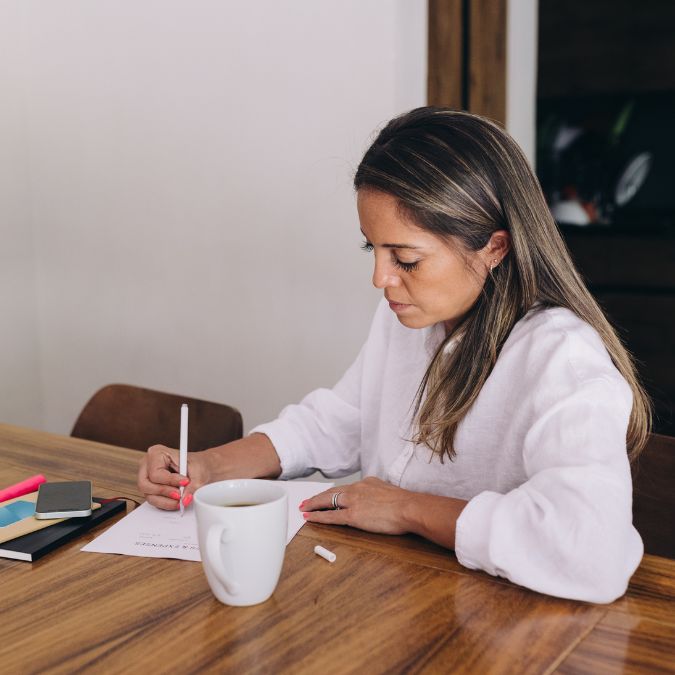 woman sitting at table writing on notepad setting money goals